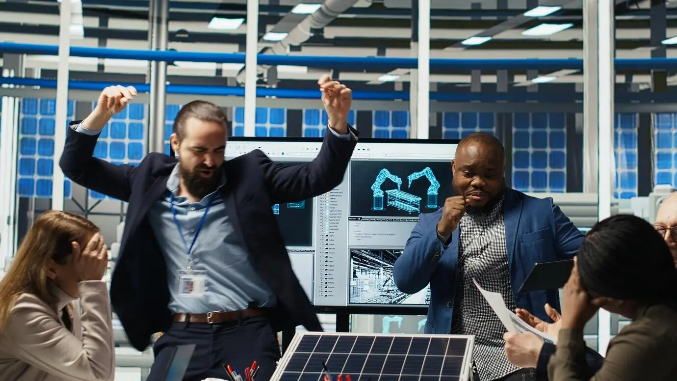 Empresarios felices en una planta de paneles solares celebran el aumento de ventas bailando.
