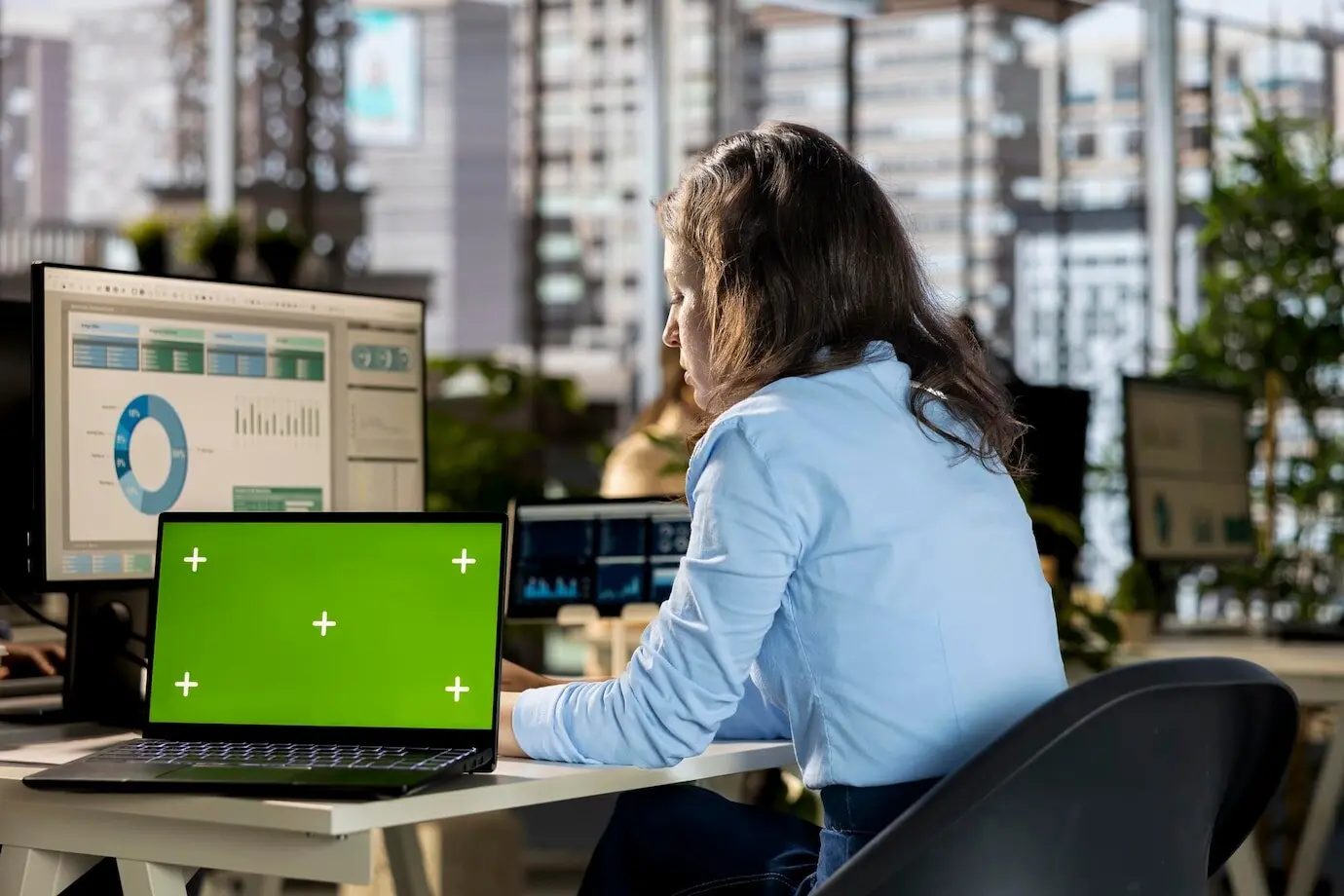 Una joven analista trabaja en informes en línea junto a una pantalla verde.